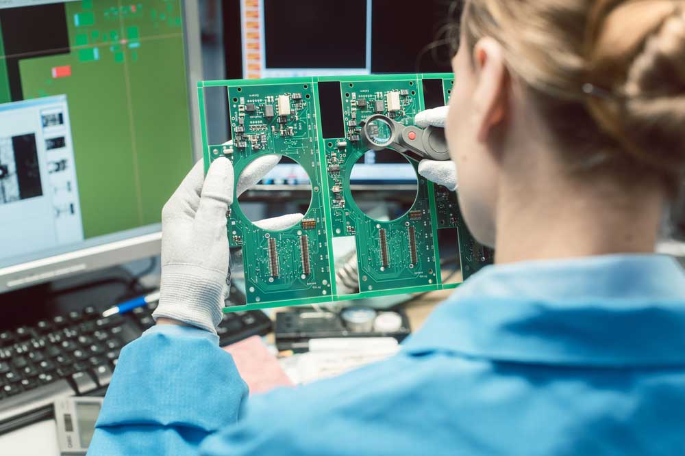 An operator visually inspects a PCB assembly